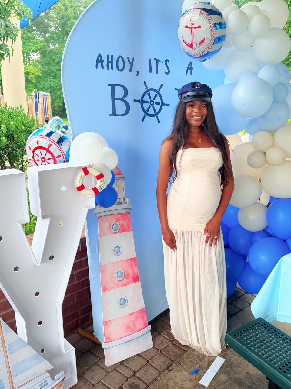 Mom-to-be posing at Ahoy It's a Boy backdrop with lighthouse prop and balloon arch